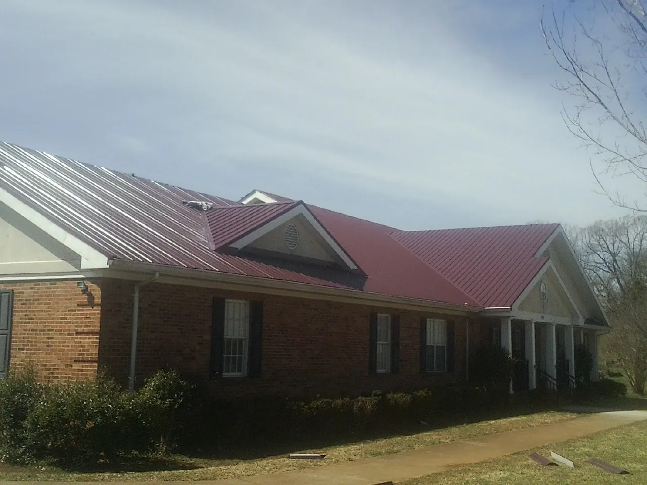 Red metal roof with gabled entries on a long brick building, from a Hail Damage Roof Repair job in Bailey