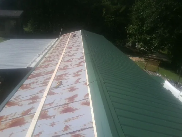 Old rusted panels beside newly installed green metal roofing — Wind Damage Roof Repair by Roofing Brothers in Bailey