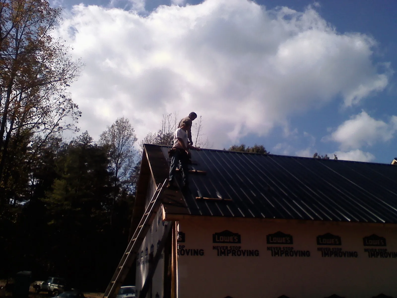 Roofer fastening dark metal panels high against a cloudy sky, from a Roof Inspection job in Bailey