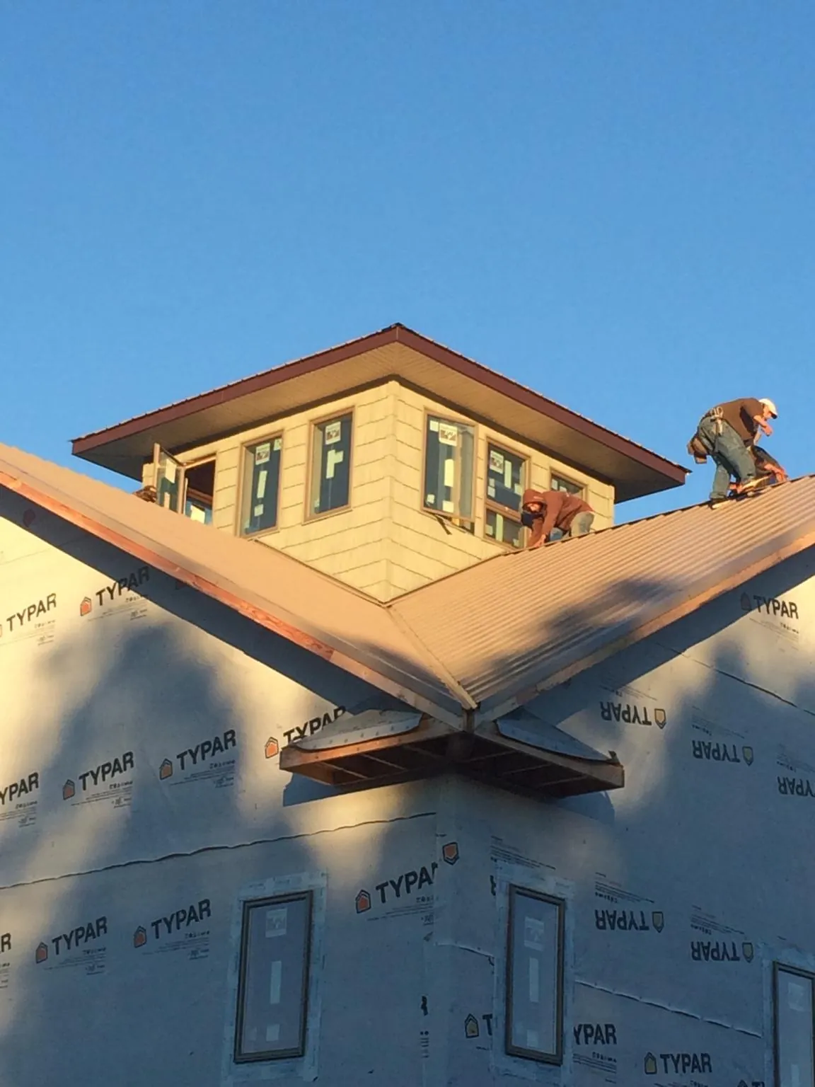 Roofers working around a rooftop cupola on a new metal roof at sunset — Roof Waterproofing in Bailey by Roofing Brothers